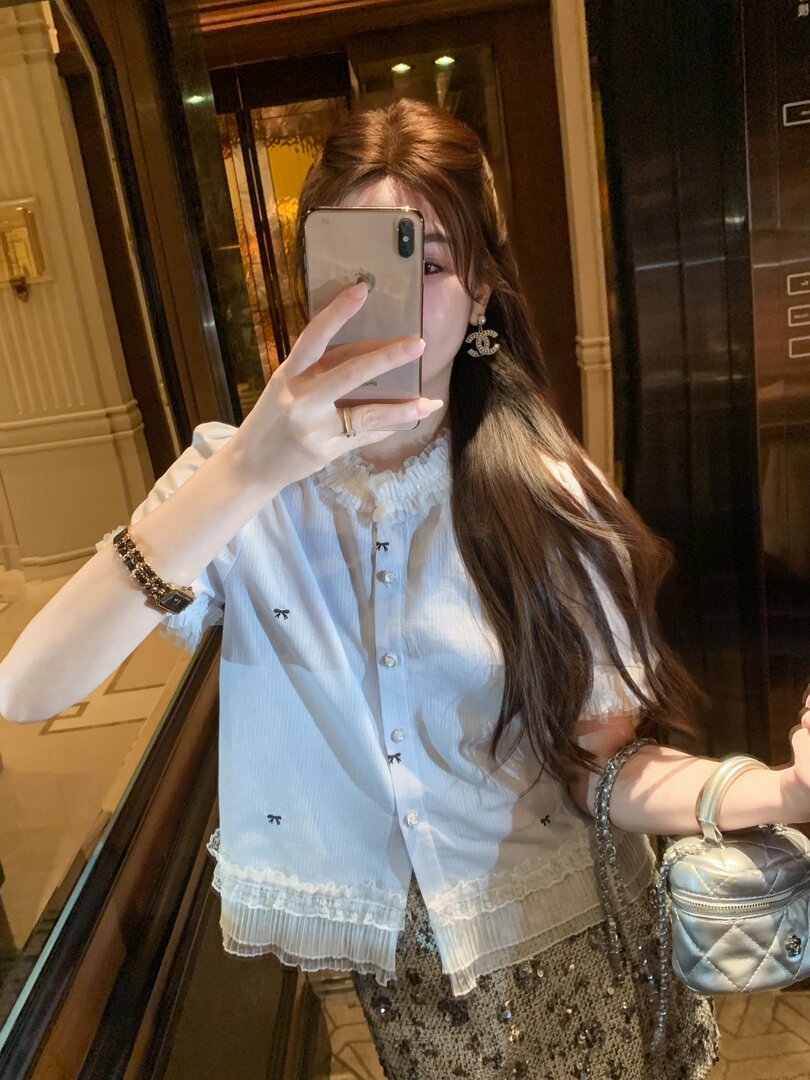 Model wearing a white ruffled short-sleeve blouse with a small quilted silver handbag