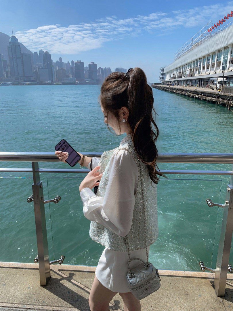 Woman wearing a white outfit and carrying a silver quilted handbag by the waterfront