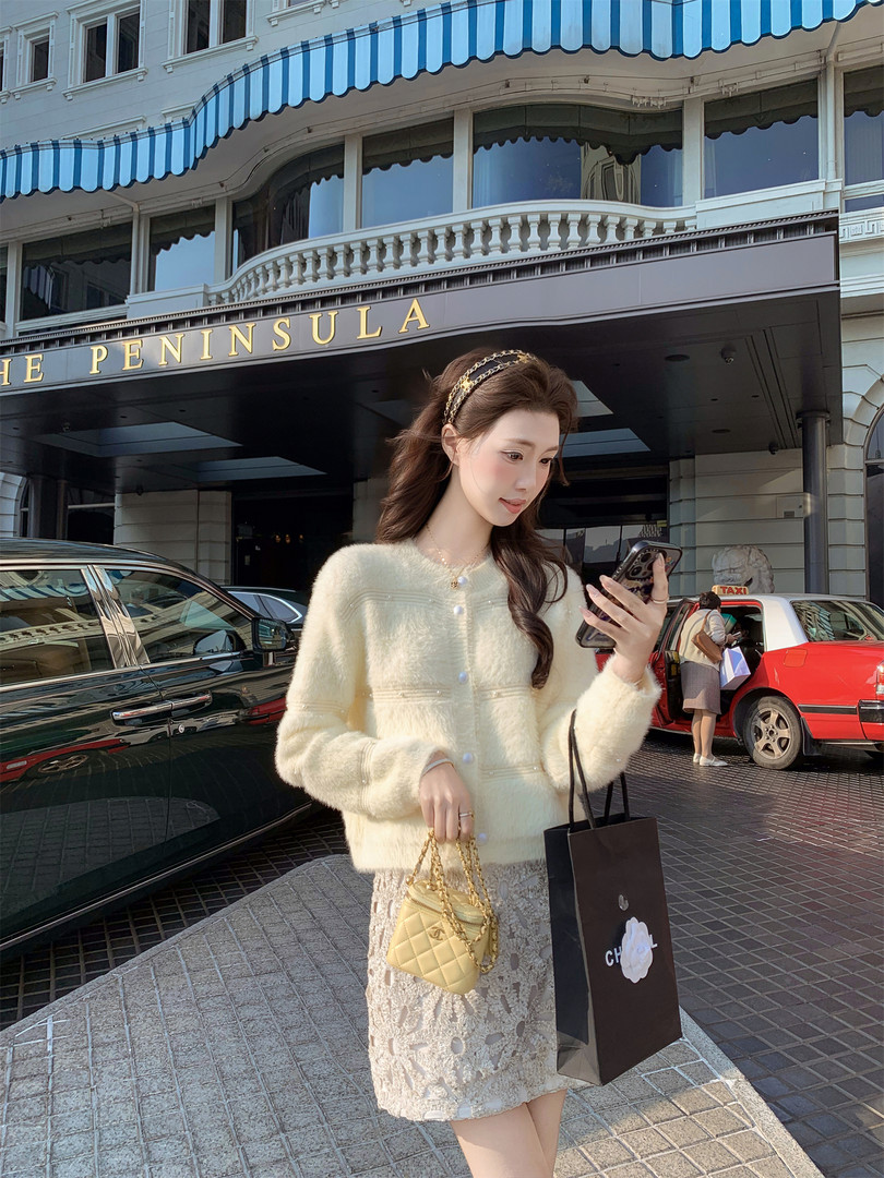 Woman wearing a cream fuzzy cardigan and lace skirt, holding a small quilted handbag outdoors