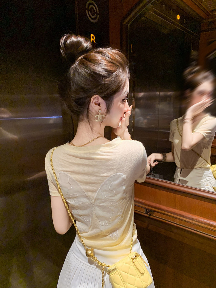 Woman wearing a beige top and carrying a small yellow quilted handbag