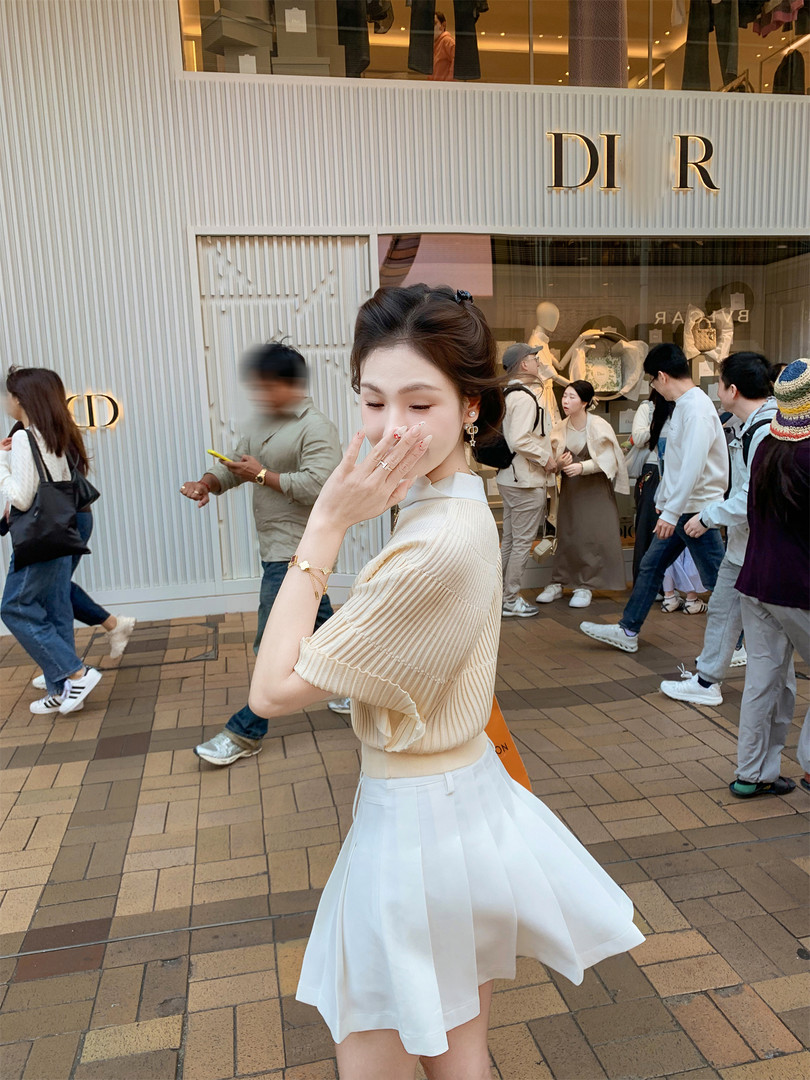 Woman wearing a cream knit top and white pleated skirt outside a Dior store