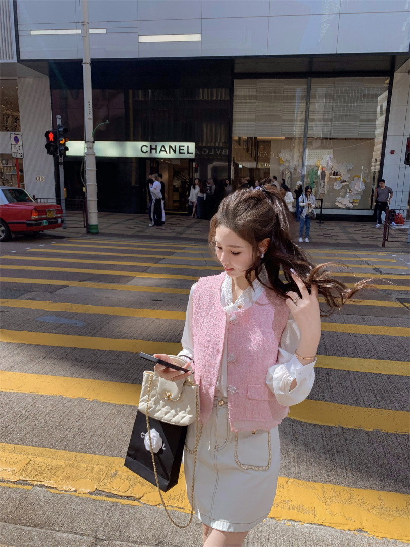 Woman wearing a pink textured vest over a white blouse and cream skirt on a city street