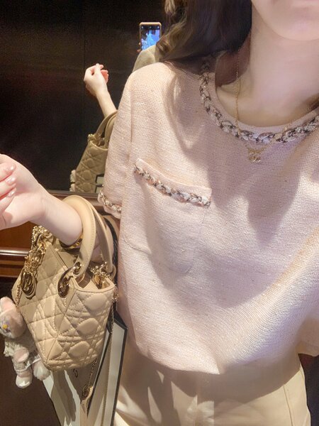 Woman wearing a light pink knit top with a quilted beige handbag