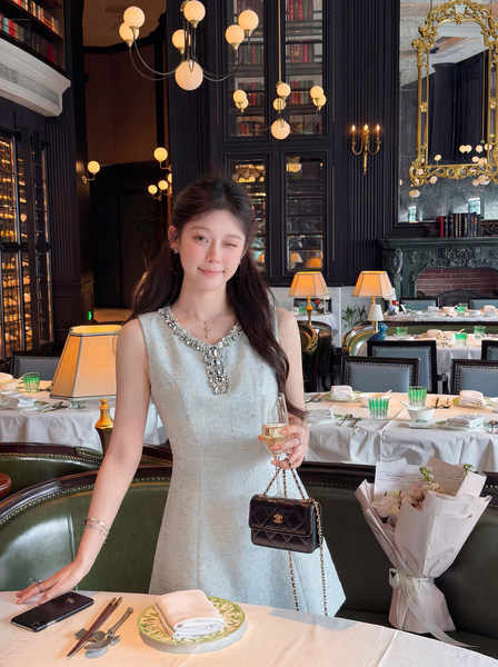 Woman wearing a light silver embellished sleeveless dress with a black quilted chain handbag