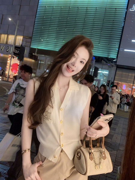Woman wearing a cream sleeveless buttoned vest and holding a beige handbag at night