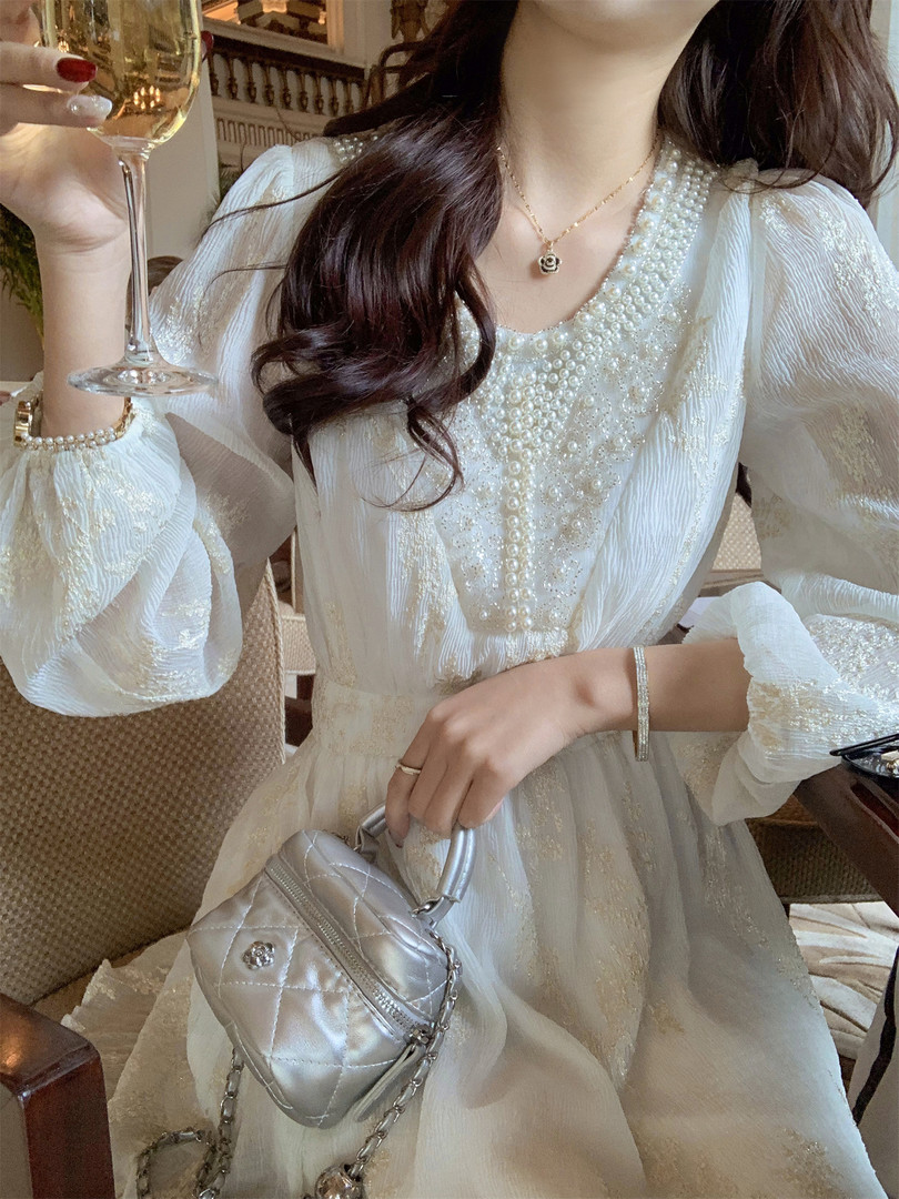 Woman wearing a white pearl-embellished dress with a silver handbag