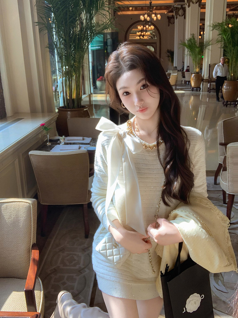 Woman wearing a cream knit dress with a large bow in a luxurious restaurant setting