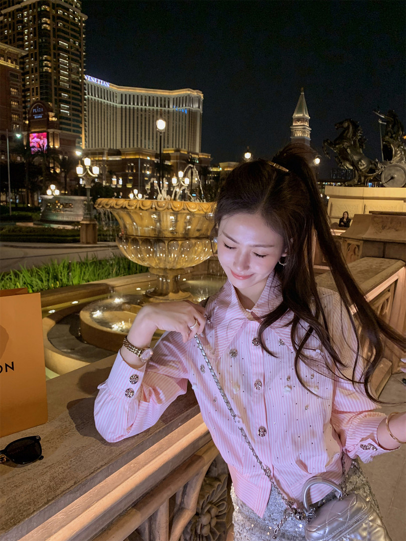 Woman wearing a pink embellished blouse with a silver chain bag at night