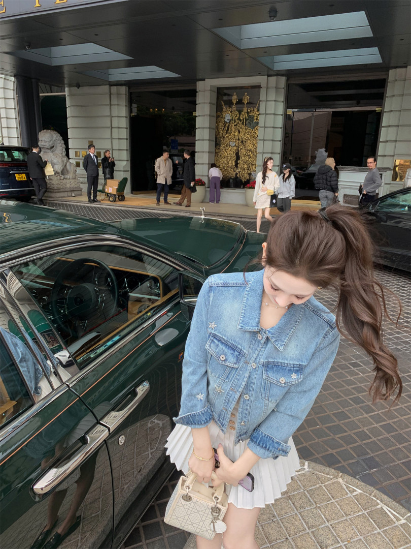 Woman wearing a light blue denim jacket with a white pleated skirt outdoors