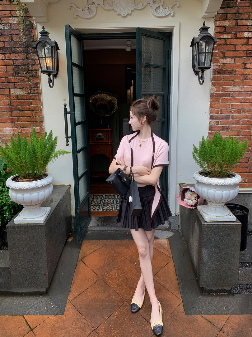 Woman wearing a pink top with a black pleated skirt and carrying a handbag