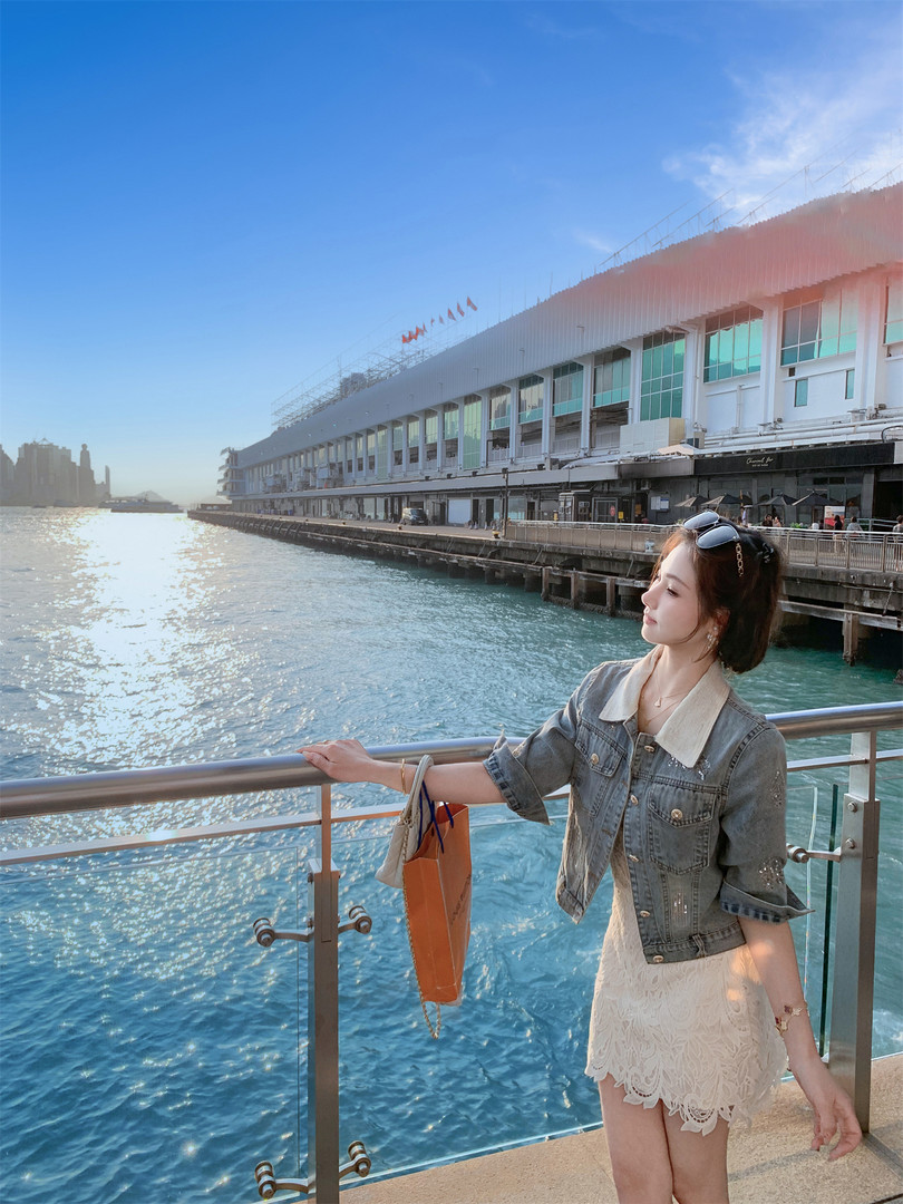 Woman wearing a denim jacket over a cream lace dress by the waterfront
