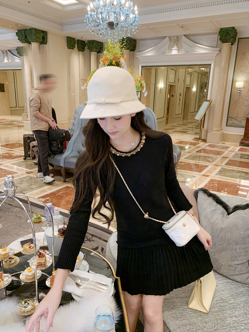 Woman wearing a black knit dress with a white hat and small white crossbody bag in a luxury hotel lobby