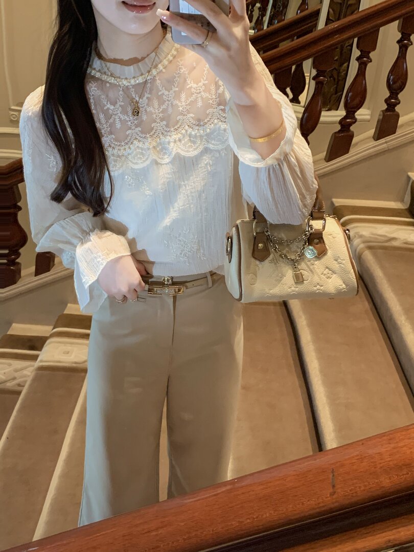 Woman wearing a white embroidered sheer blouse with beige wide-leg pants and a cream handbag