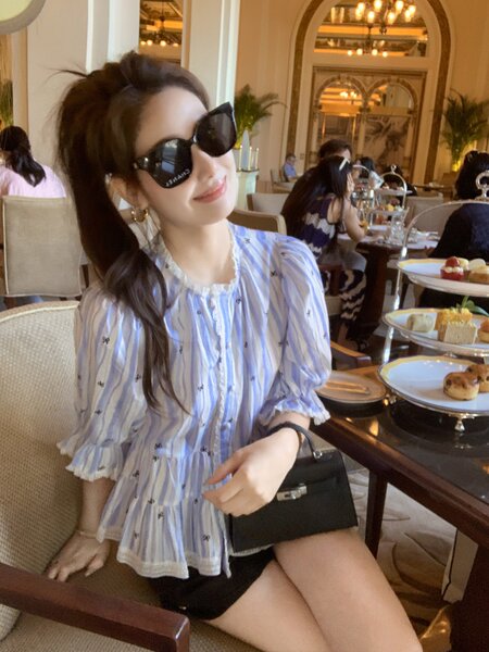 Woman wearing a light blue striped puff-sleeve blouse with black shorts and sunglasses