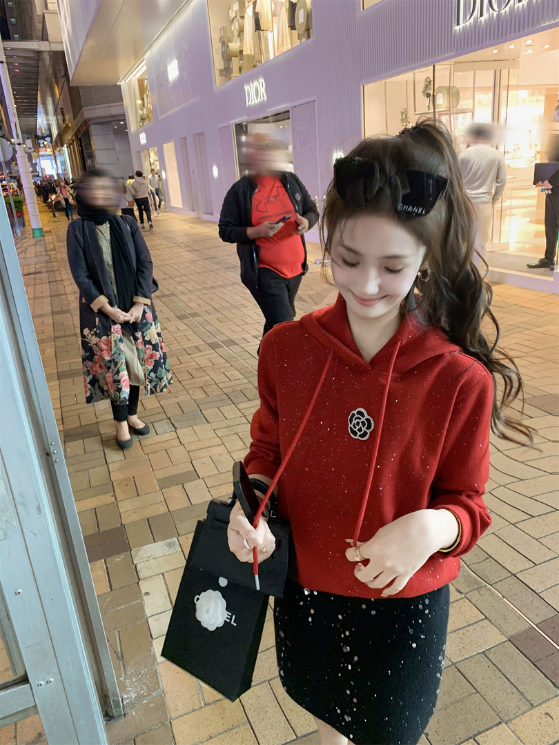 Woman wearing a red hooded sweatshirt and black skirt while holding a shopping bag outside a Dior store