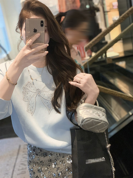 Woman wearing a light blue embellished top with a sequined skirt and quilted mini bag