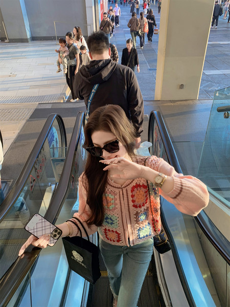 Woman wearing a pink crochet cardigan and jeans on an escalator