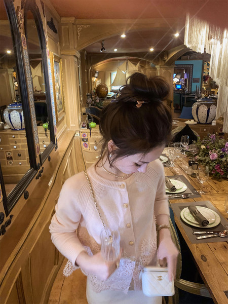 Woman wearing a light pink lace-trim cardigan and carrying a white purse in a restaurant