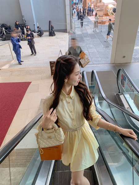 Woman wearing a pale yellow dress with a quilted handbag on an escalator