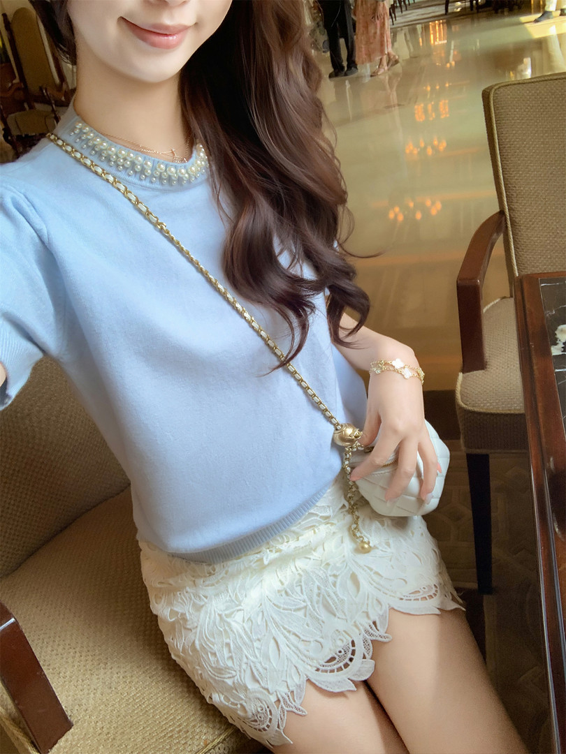 Woman wearing a light blue pearl-embellished top with a white lace skirt