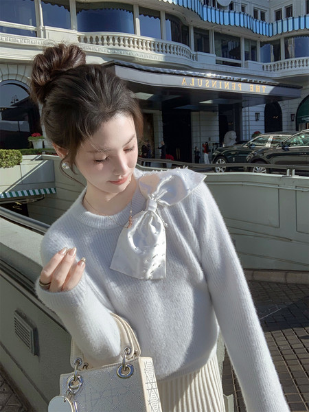 Woman wearing a white fuzzy sweater with a satin bow detail and a cream handbag