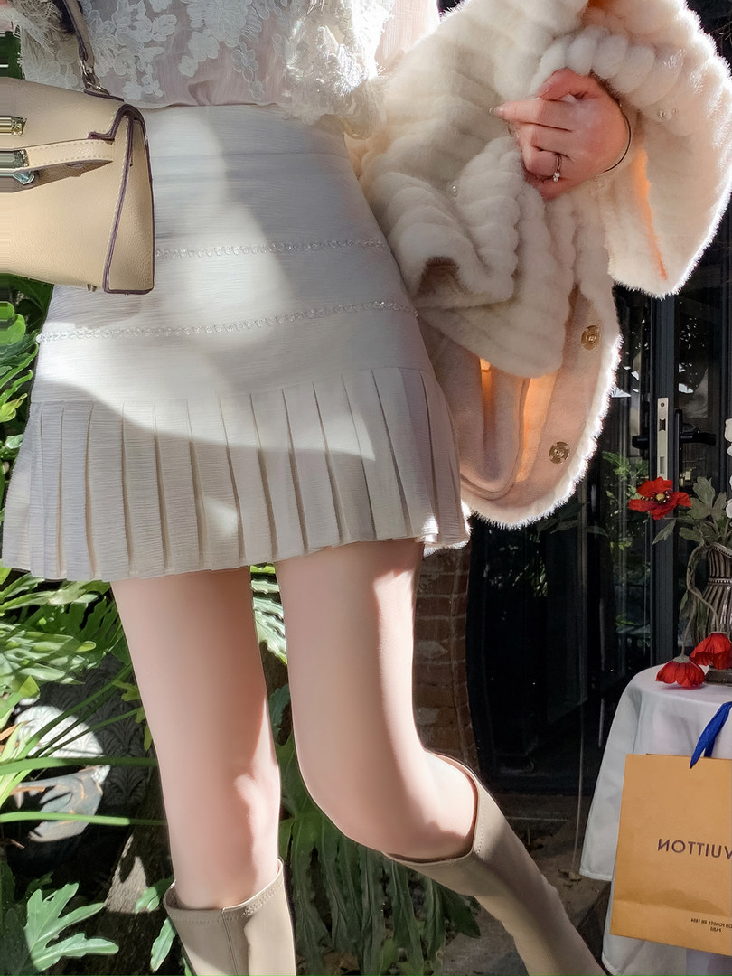 Model wearing a light pleated skirt with a fluffy cream coat and beige boots