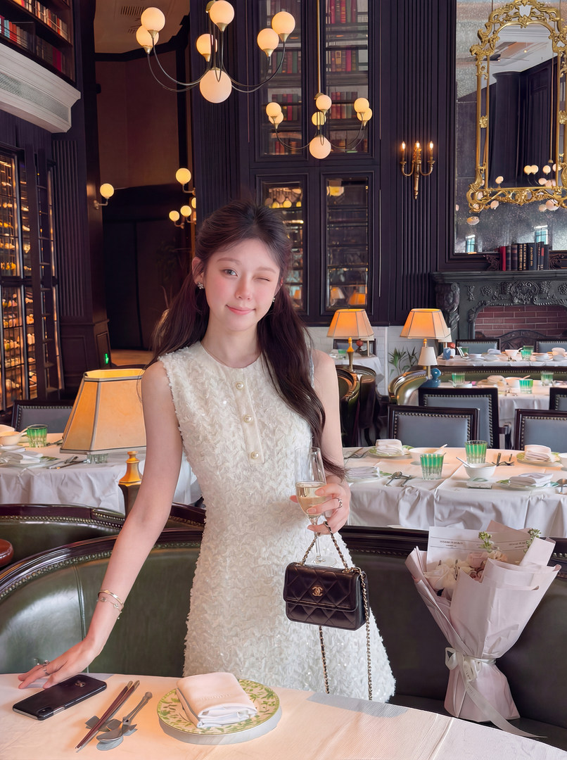 Woman wearing a white textured sleeveless dress and holding a black quilted chain bag in a restaurant