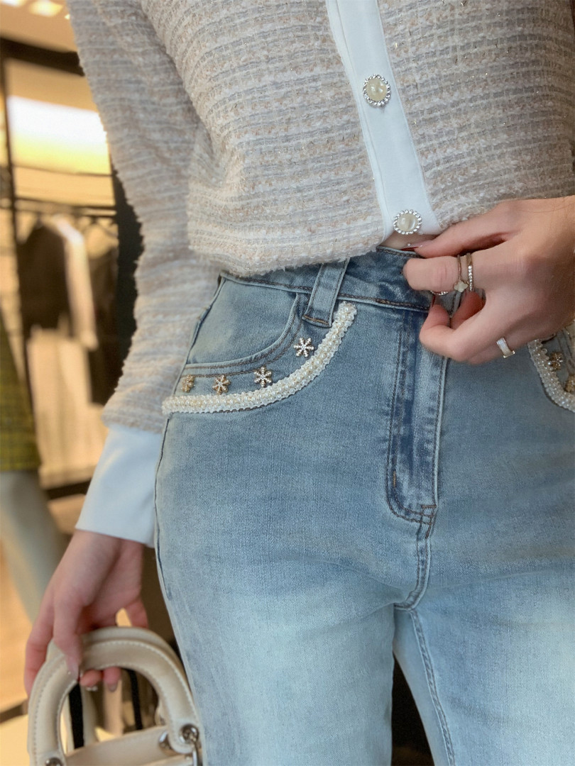 Model wearing light blue embellished jeans with a textured cardigan and holding a handbag