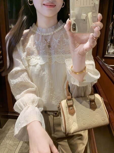 Woman wearing a white embroidered blouse and holding a beige handbag