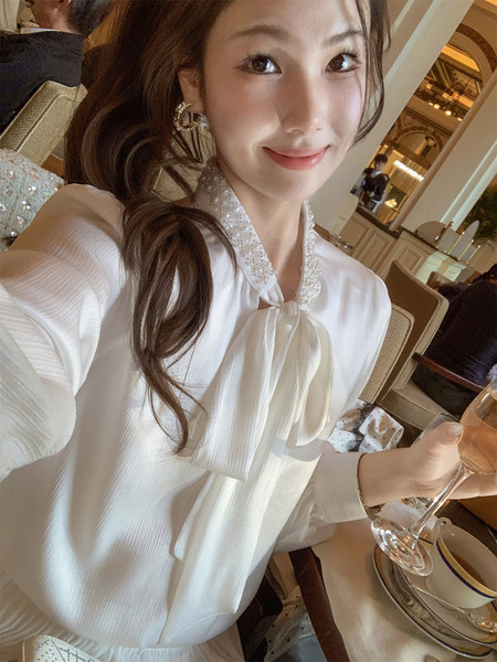 White long-sleeve blouse with pearl-trimmed collar and bow tie worn by a model