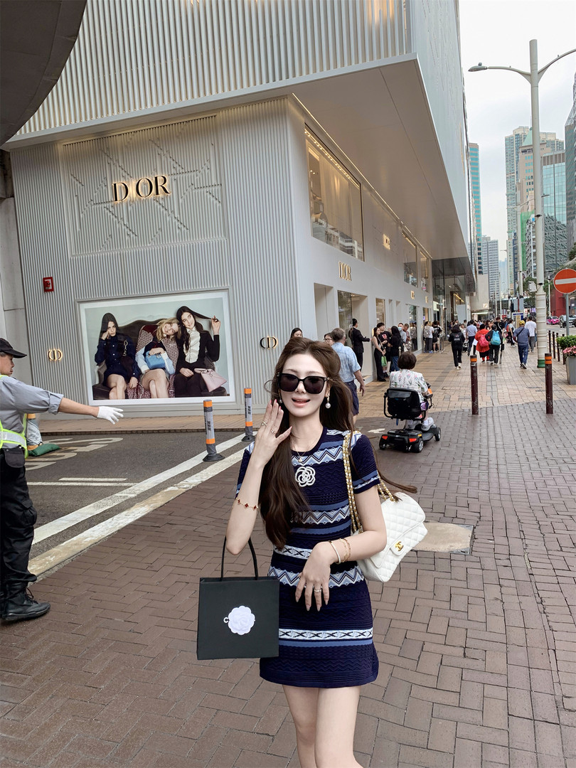 Woman wearing a navy patterned dress with a white quilted handbag outside a Dior store