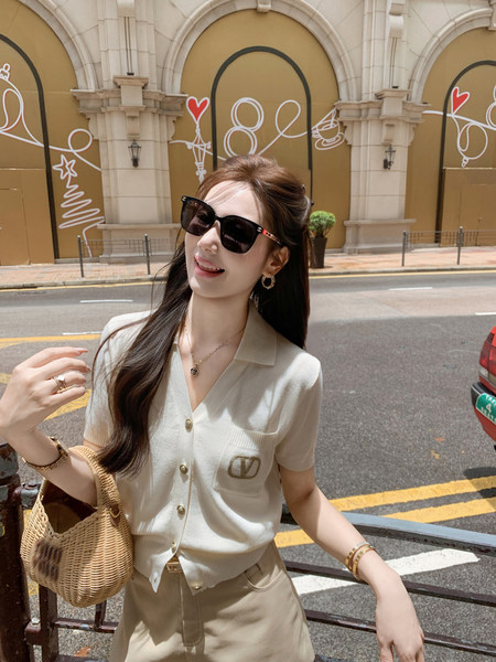 Woman wearing a cream short-sleeve knit button-up top with a woven handbag