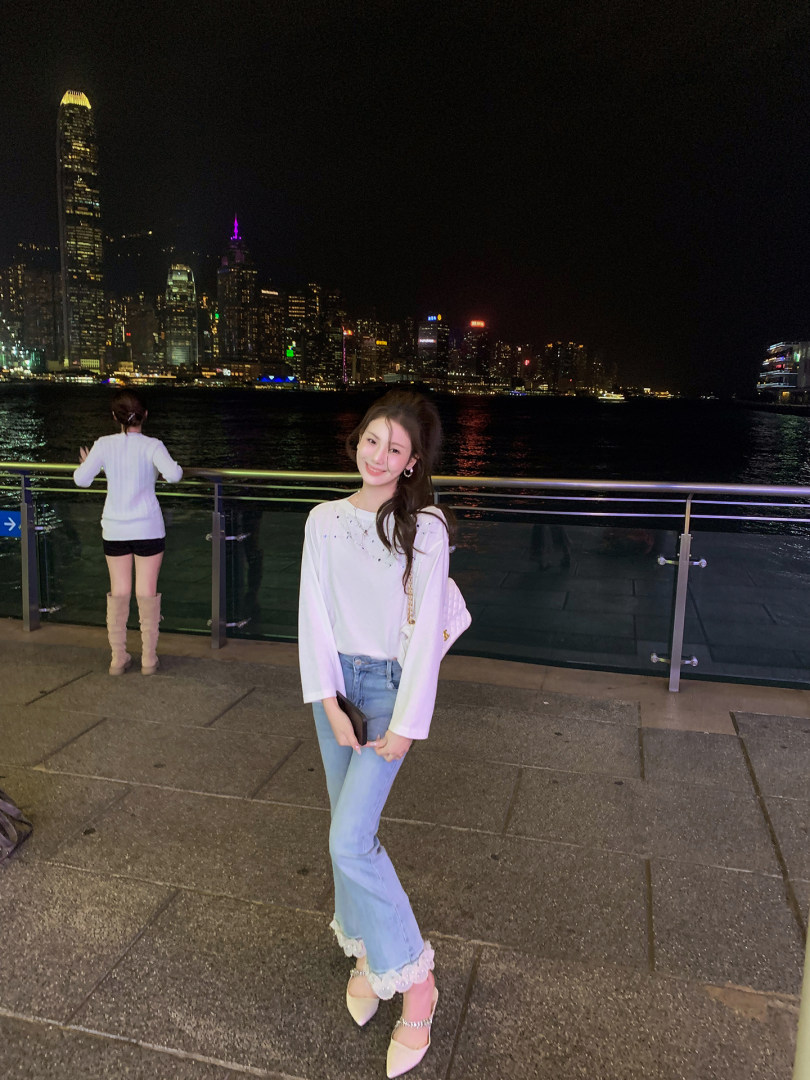 Woman wearing a white top with light blue jeans and heels at night by the waterfront