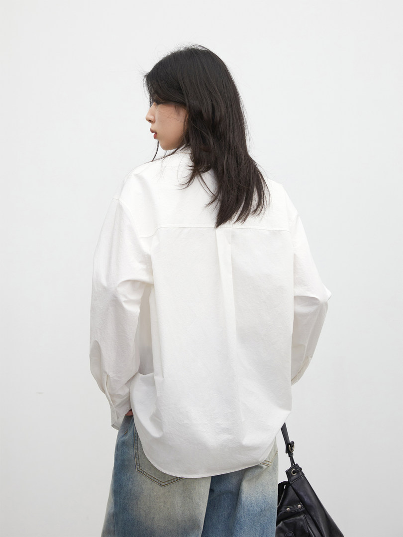 Model wearing an oversized white long-sleeve shirt with jeans and a black shoulder bag