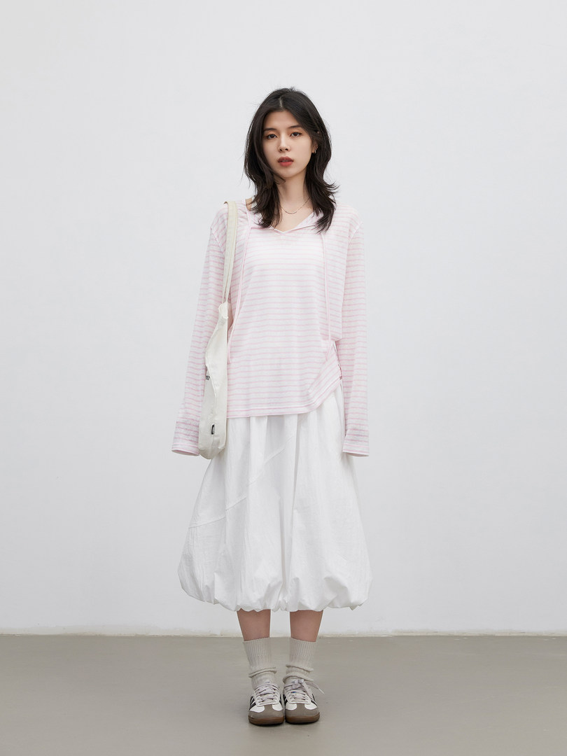 Model wearing a pink striped long-sleeve top with a white skirt and sneakers