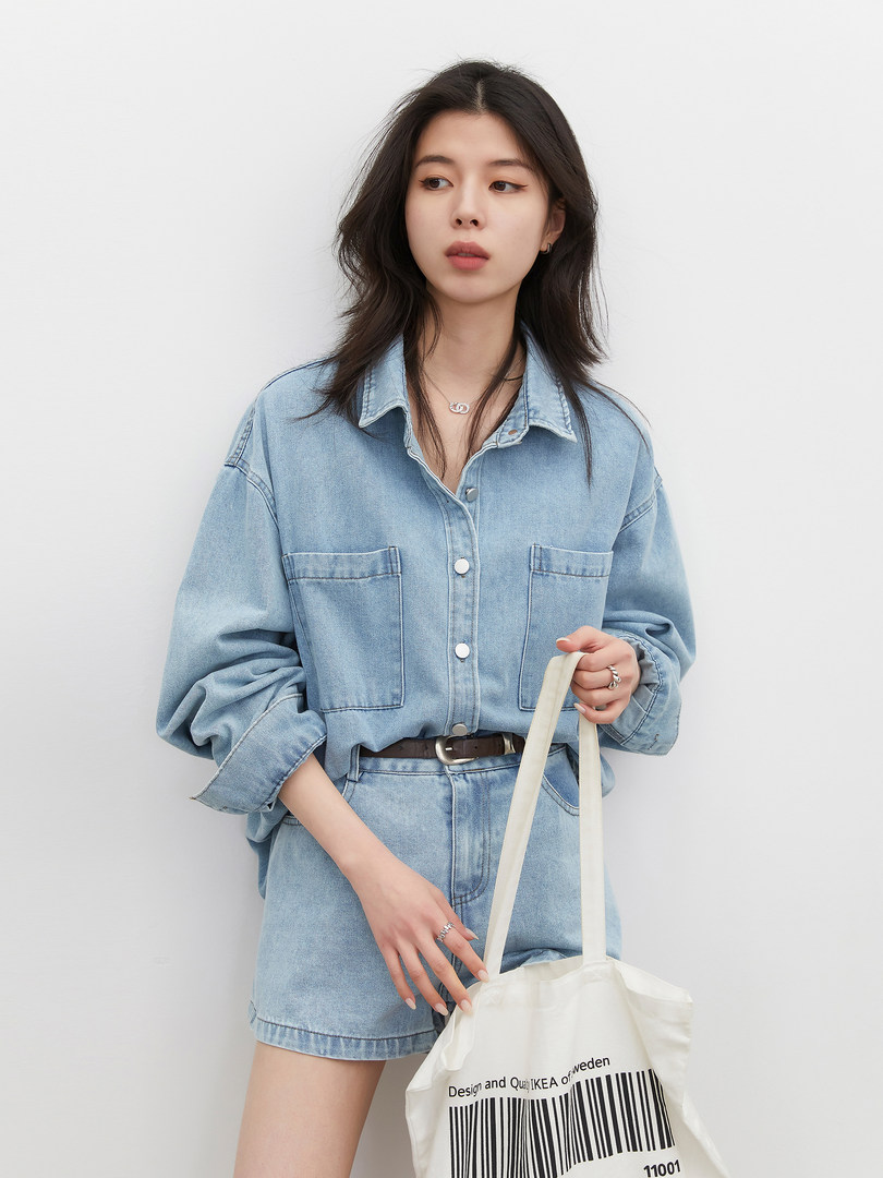 Model wearing a light blue denim shirt-and-shorts outfit holding a tote bag