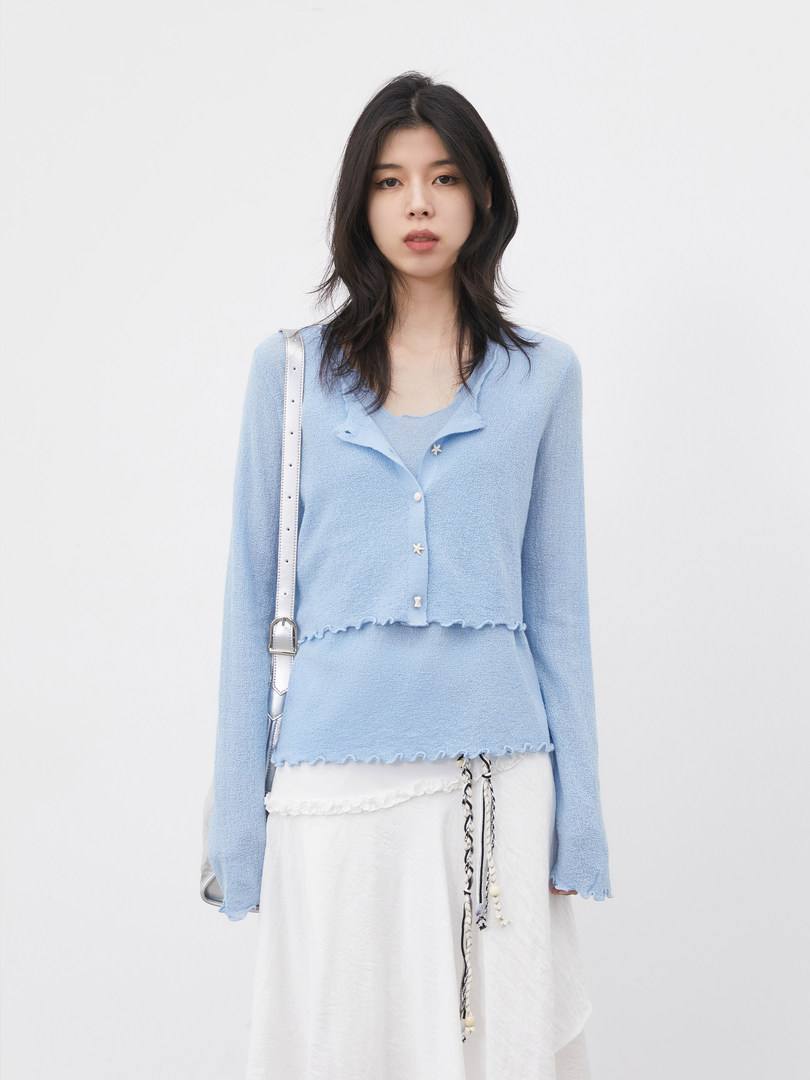 Model wearing a light blue knit cardigan layered over a matching top with a white skirt