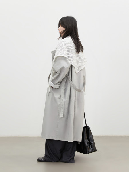 Model wearing a light gray long trench coat with layered styling and a black tote bag