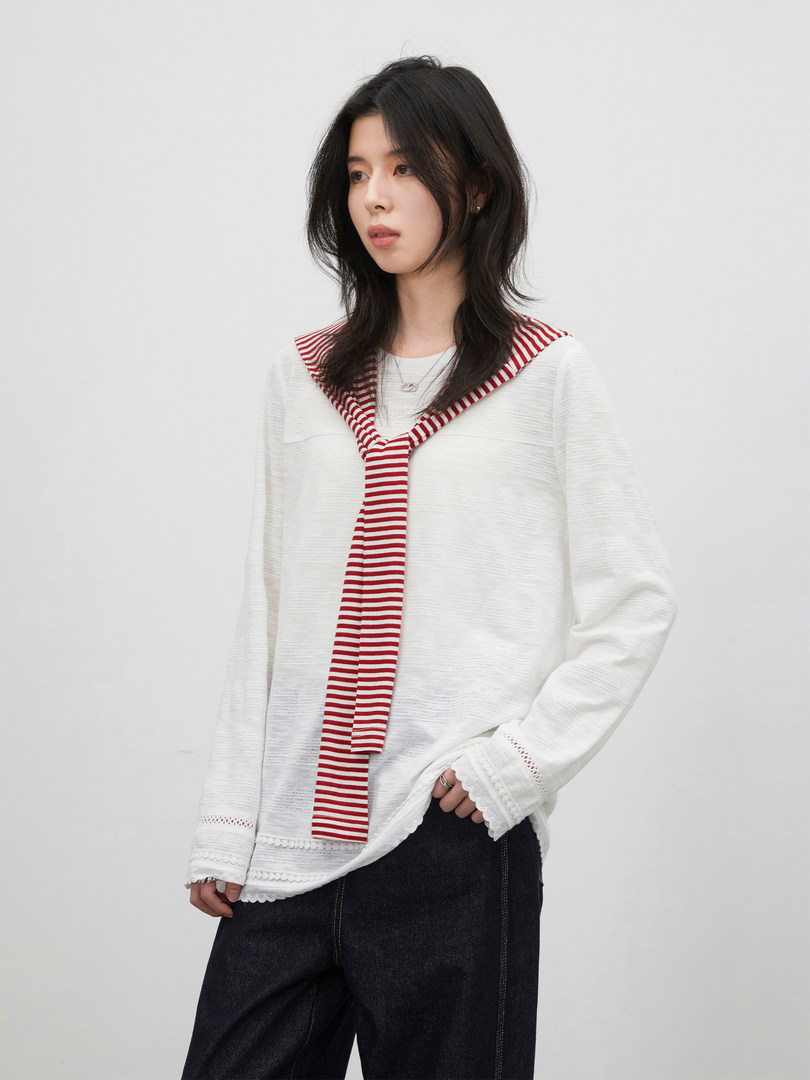 Model wearing a white long-sleeve top with a red striped scarf detail and dark pants