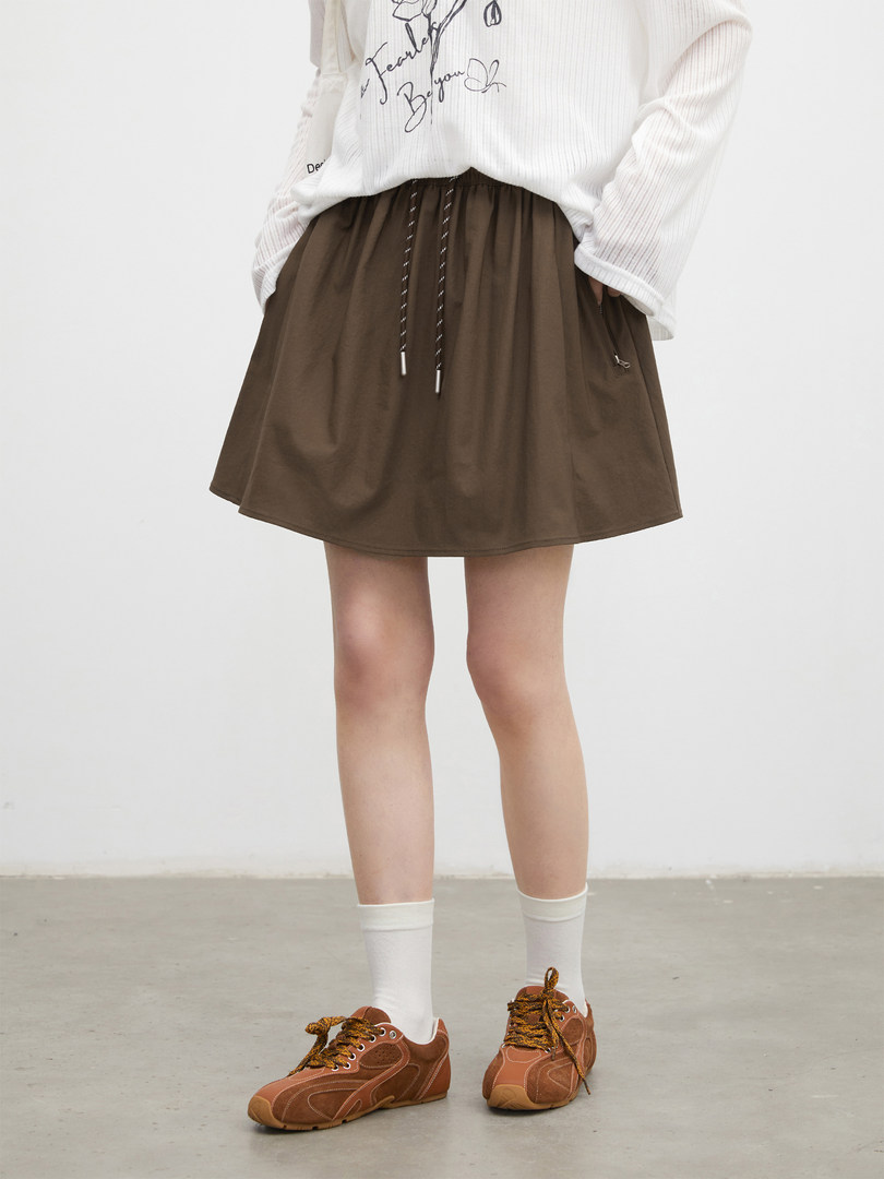 Model wearing a brown drawstring skirt with a white graphic top and sneakers