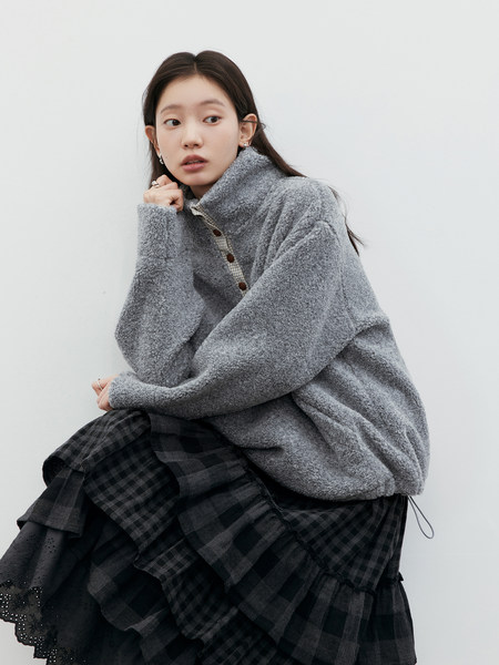 Model wearing a gray textured pullover sweater with a black plaid skirt