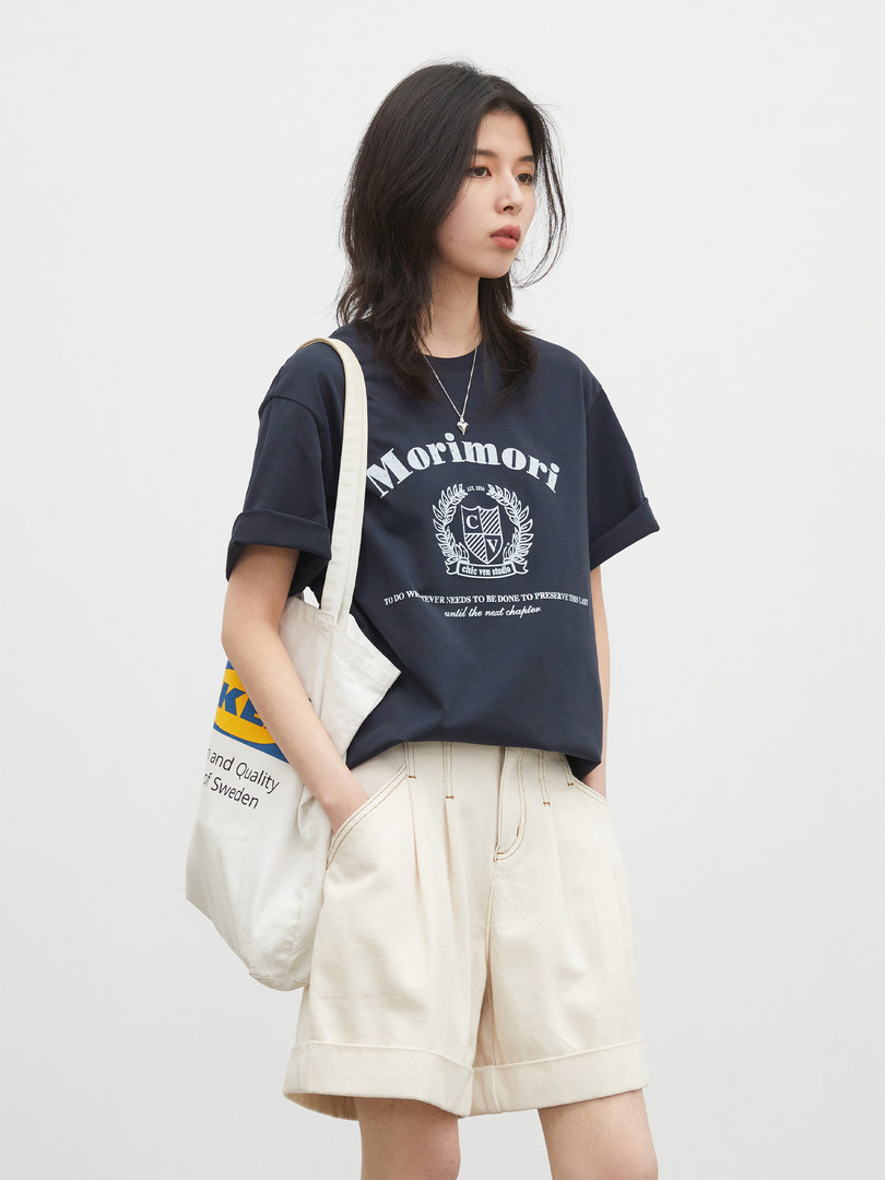 Model wearing a navy graphic t-shirt with cream shorts and a tote bag