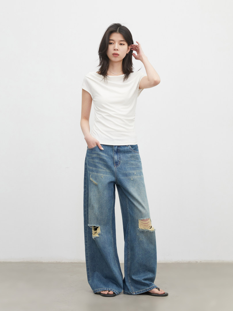 Model wearing a white short-sleeve top and distressed wide-leg blue jeans