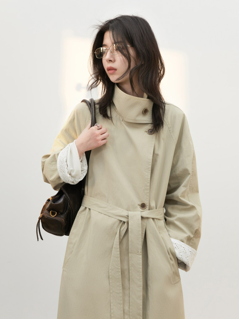 Model wearing a beige belted trench coat with a high collar and buttons