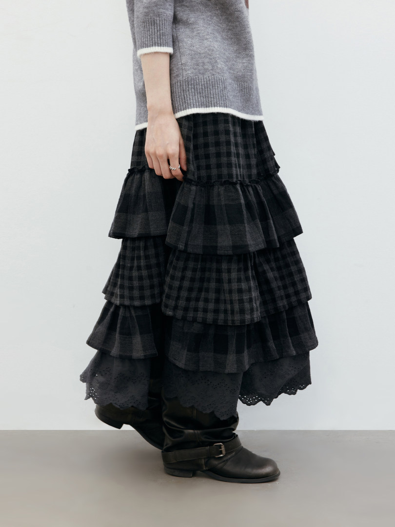 Model wearing a layered black plaid skirt with black boots and a gray sweater