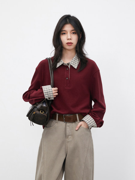 Model wearing a burgundy long-sleeve polo shirt with plaid collar and cuffs, paired with wide-leg pants and a shoulder bag