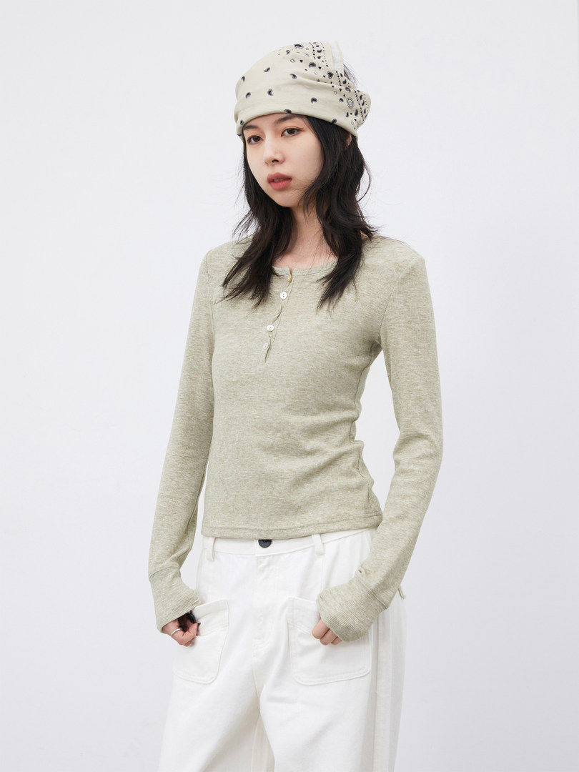 Model wearing a beige fitted long-sleeve top with white pants and a bandana-style hat