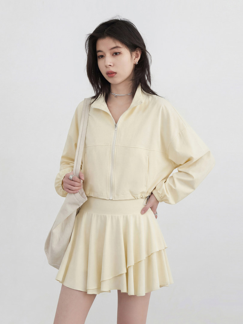 Model wearing a light yellow zip-up jacket and matching layered skirt