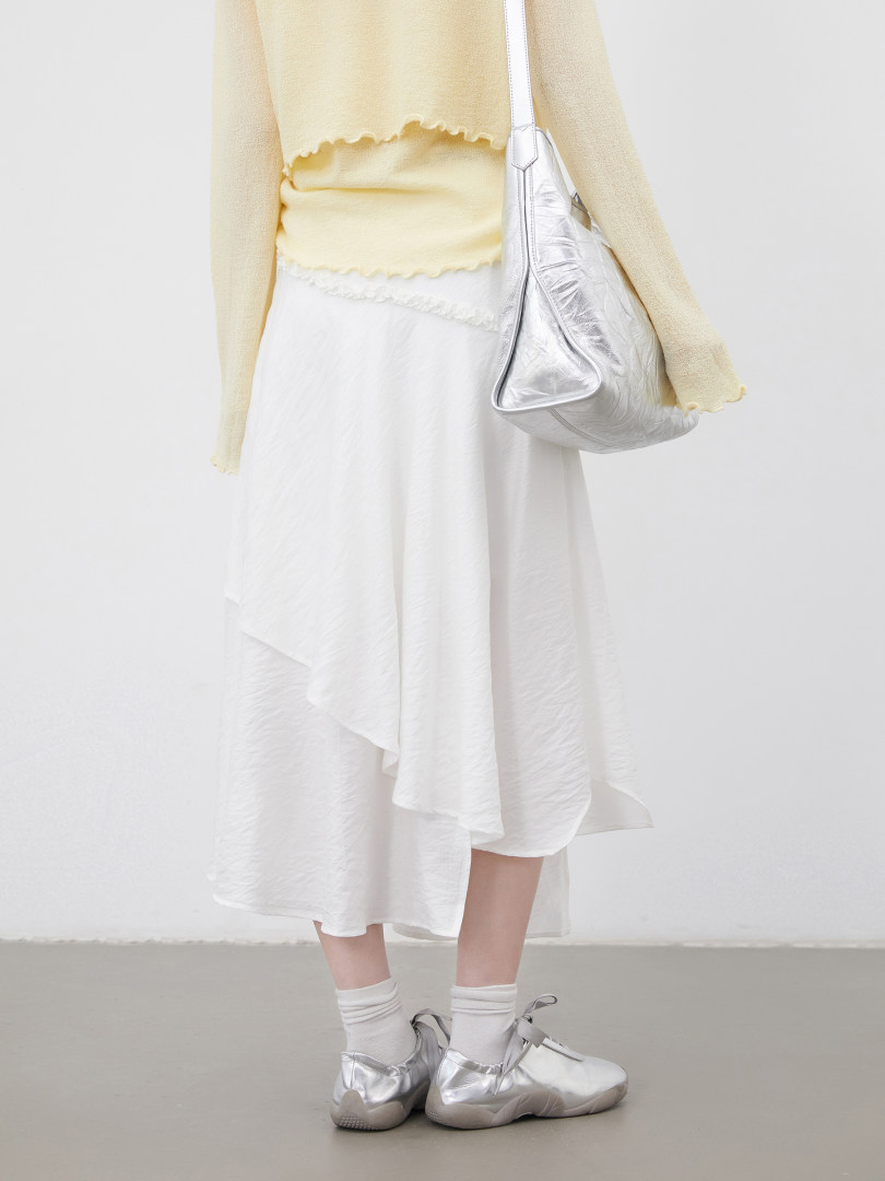 Model wearing a light yellow top with a white asymmetrical skirt, silver sneakers, and a metallic shoulder bag