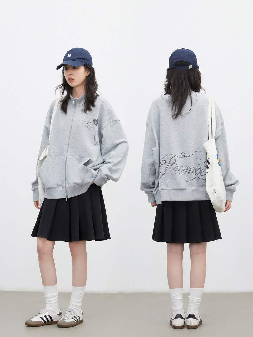 Model wearing a gray oversized zip-up sweatshirt with a black pleated skirt and baseball cap